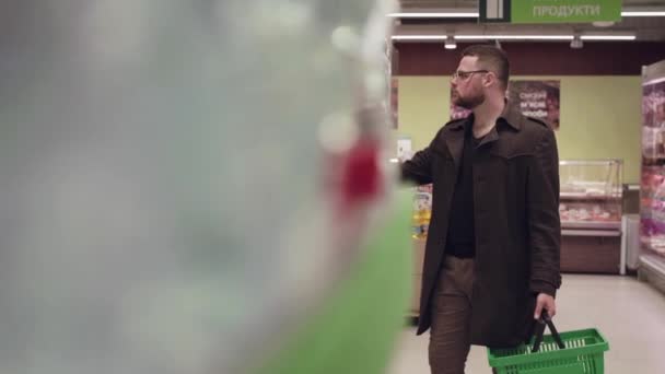 O homem olhando prateleiras de supermercado e colocando mercadorias em cesta — Vídeo de Stock