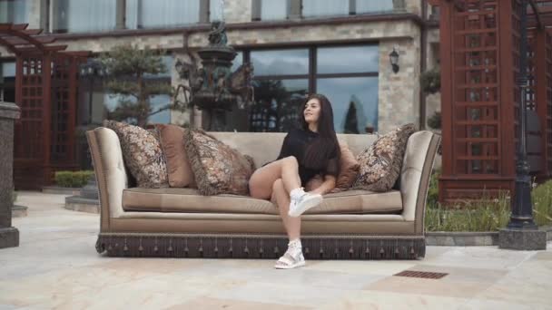 Ardent long-haired brunette differently relaxes and poses on a sofa outdoors — Stock Video