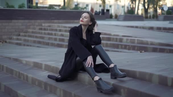 Stylish model with red lips and black clothes poses on street stairs — Stock Video