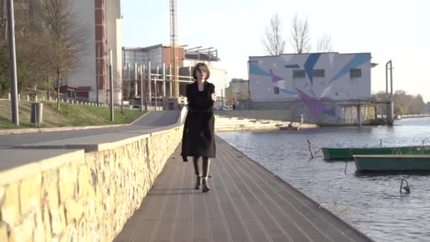 Bedachtzame brunette met kronkelende haren wandelingen in jas aan het meer van de stad — Stockvideo