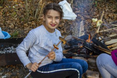 Kız ormanda ateşte ekmek kızartıyor.