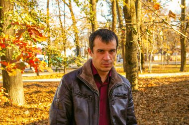 Genç adam sonbahar parkında sonbahar oyuncularının arka planında duruyor..