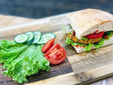 Taze ızgara sandviç tahtanın üzerinde duruyor. Amerikan mutfağı yemekleri. Biftek ve dilimlenmiş büyük sandviç, salata, salatalık, yakın plan domates. Sokak yemeği, fast food..