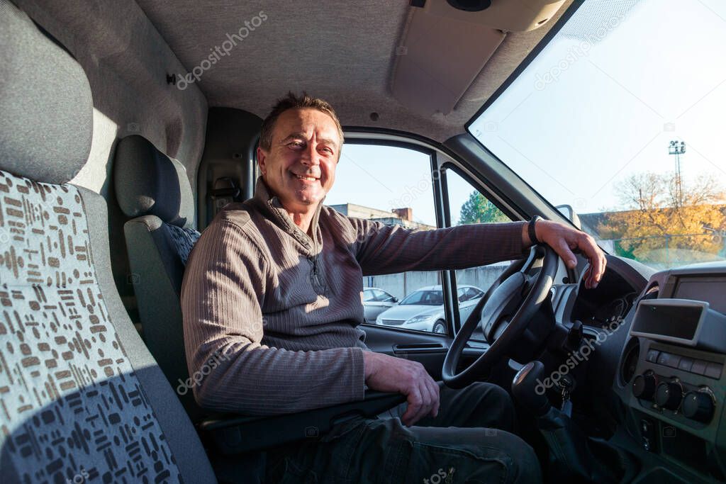A man driver is sitting in the cab of a modern truck.