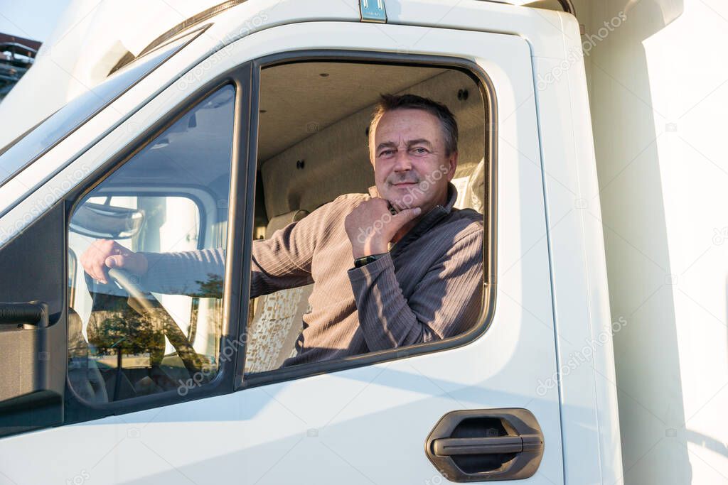 A man driver is sitting in the cab of a modern truck.