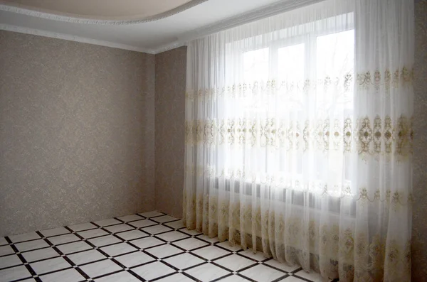 Classic empty interior with a light wall, tiles on the floor, window and curtain.