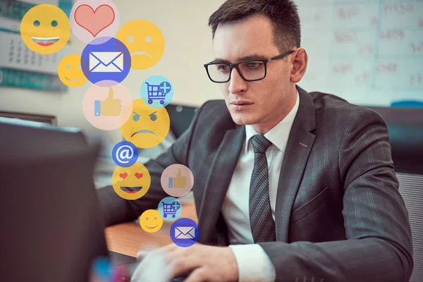 Closeup portrait of a young male businessman, happy working with a phone with a laptop holding a mouse in his hands. Emoticons of social networks go up.