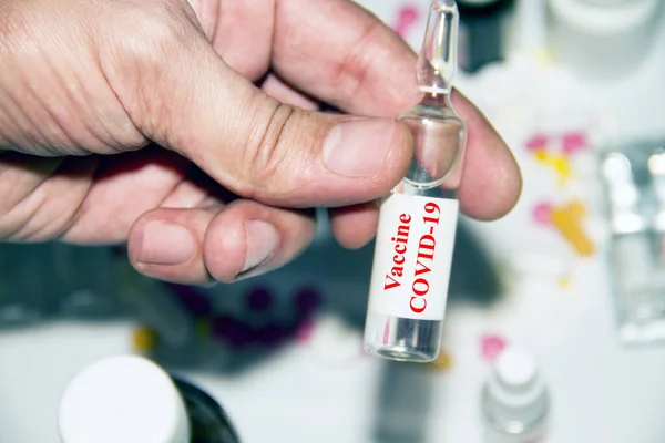 研究室の医師は ラベルと異なる薬の背景にCovid 19ワクチンの碑文を持つアンプルを手に持っています — ストック写真