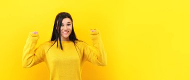 Kız, başarısını ve zaferini kutluyor. Yumruklarını neşeyle sıkıyor. Sarı kazaklı şanslı kadın kameraya gülümsüyor, panoramik model