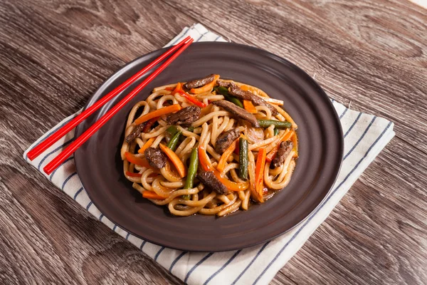 Noodles with beef and vegetables, black mushrooms in a dark plat — Stock Photo, Image