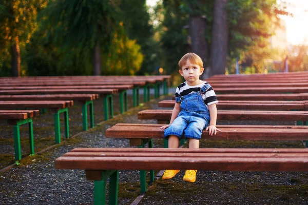 Мальчик сидит на скамейке и что-то думает. — стоковое фото