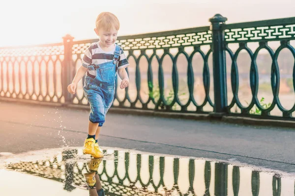 Мальчик бежит через лужи в переулке парка в четные — стоковое фото