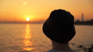 Gün batımında, deniz kenarında genç adam rahatlatıcı Eller başının arkasında, hepsini almak.