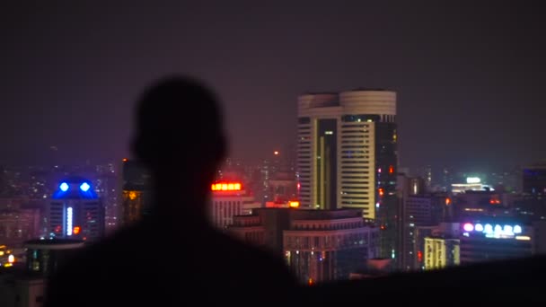 Um homem no topo de um edifício à noite olhando para a cidade — Vídeo de Stock