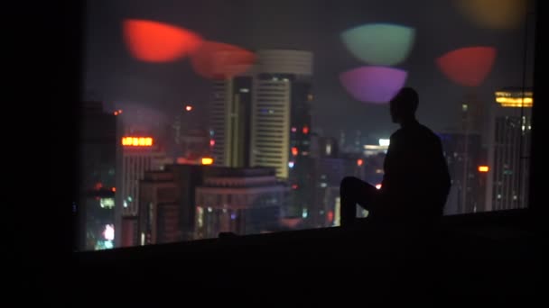 Um homem no topo de um edifício à noite olhando para a cidade — Vídeo de Stock