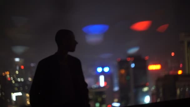 Un hombre en la parte superior de un edificio en la noche mirando a la ciudad — Vídeos de Stock