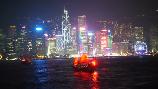 Hongkong-Blick in der Nacht vom Viktoria-Hafen mit traditionellem rotem Segel-Schrottboot und modernen Wolkenkratzern und anderen städtischen Gebäuden des Finanzbezirks der Stadt — Stockvideo