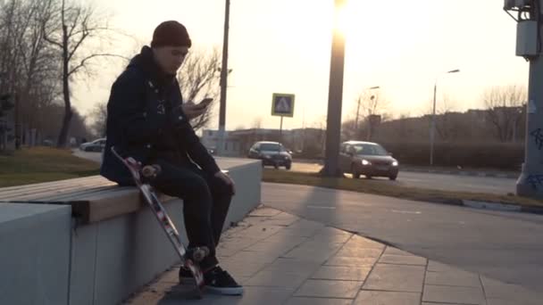 Attractive man relaxing with a skateboard and texting — Stock Video