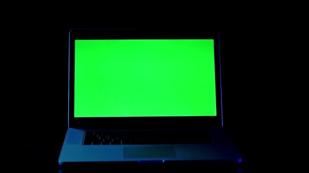 Laptop med grön skärm i neonljus på svart bakgrund Mörkt kontor. — Stockvideo