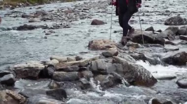 Sırt çantası olan ve iz sürmek için sopa kullanan gezgin kadın bir dağ deresinden geçiyor..