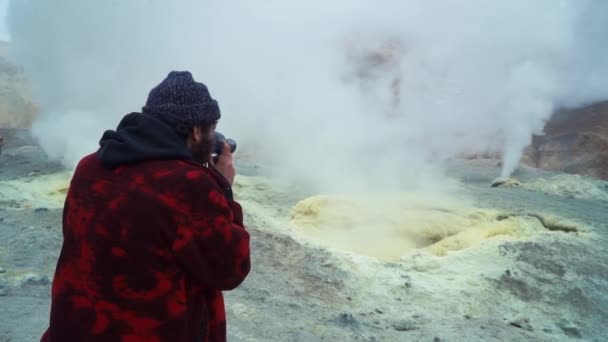 Een jonge baard hipster blogger Wandelen op de top van een vulkaan en het opnemen van video 's van gas en rook. Kamtsjatka Rusland — Stockvideo