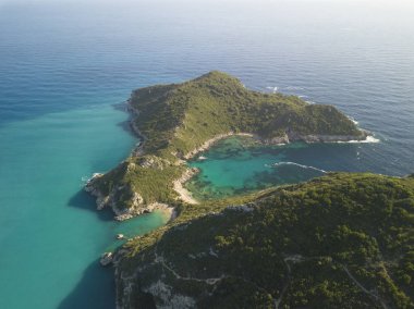 Yunanistan 'ın Korfu Adası' ndaki popüler gençlik plajından hava manzarası. Gerçekçi olmayan bir şekilde canlı suyla çevrili çift aynalı körfez sahili.