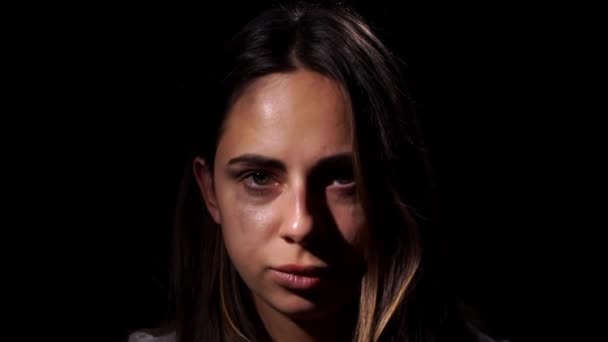 A tearful and frightened sad girl looking in the camera on black background. Domestic violence and social problems concept. Close up — Stockvideo