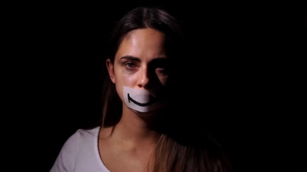 Huiselijk geweld en sociaal probleemconcept. Wanhopige vrouw in depressie kijkt naar de camera en zet een glimlach afbeelding op haar gezicht op zwarte achtergrond — Stockvideo