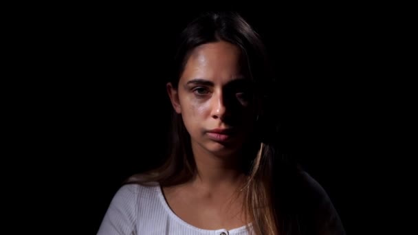 Domestic violence and social problems concept. A sad woman puts dark glasses to close bruises on her face on a black background — Stockvideo