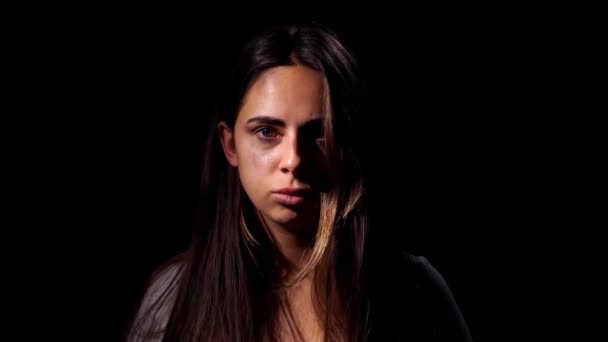 A tearful and frightened sad girl looking in the camera on black background. Domestic violence and social problems concept — Stockvideo