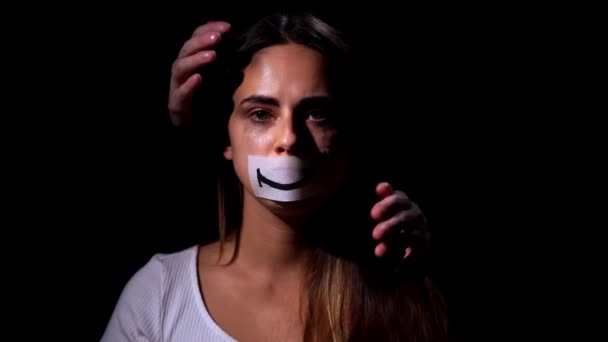 Domestic violence and social problems concept. Desperate woman in depression looks at the camera and puts a smile image on her face on black background — Stock Video