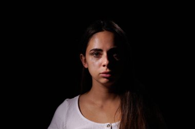 Gözü yaşlı ve korkmuş üzgün bir kız siyah arka planda kameraya bakıyor. Aile içi şiddet ve sosyal sorunlar kavramı