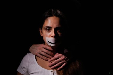 Aile içi şiddet ve sosyal sorunlar kavramı. Depresyondaki umutsuz kadın kameraya bakar ve yüzüne siyah arka planda bir gülücük koyar.