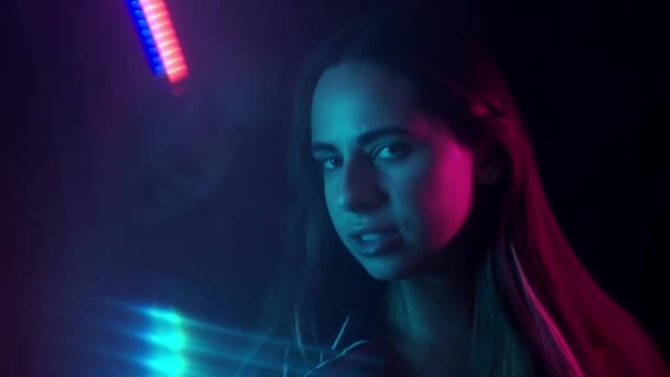Neon ışıklarının arasında durup kameraya bakan güzel genç kadının portresi. Neon ışıkları — Stok video