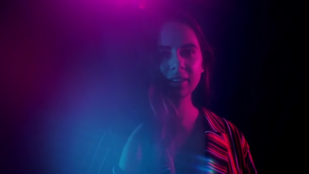 Neon ışıklarının arasında durup kameraya bakan güzel genç kadının portresi. Neon ışıkları — Stok video