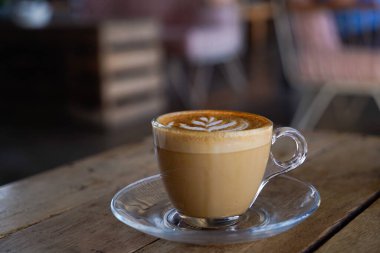Arka planda bulanık duran bir kahve dükkanının ahşap masasında bir fincan sıcak kapuçino. Bali Canggu 'da ünlü bir yer.