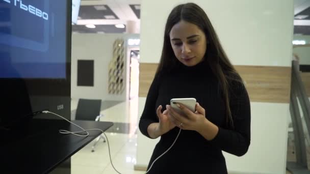 Kadın havaalanında telefon kullanıyor ve şarj ediyor. Bir kadın şarj istasyonunun yanında duruyor ve telefonu şarj ediyor.. — Stok video