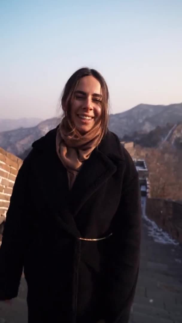 Mujer feliz caminar en la Gran Muralla de China, bajar de la torre de vigilancia en la sección Badaling al atardecer en invierno. Vídeo vertical — Vídeo de stock