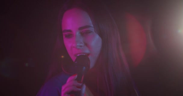 Fille élégante joyeuse chantant et souriant dans les néons sur un fond noir 