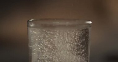 Fışkırtan aspirin tableti bir bardak suya düşüyor, yavaş çekimde köpüren haplar kapanıyor ve kabarcıklarla çözülüyor. İlaç, sağlık eczanesi kimya konsepti