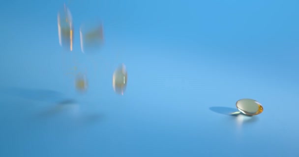 Slow motion shot van vallende Omega 3 Fish Oil capsules op blauwe achtergrond. Gouden kleur vitaminen in gel shell. Gezondheidszorgconcept. Farmaceutische industrie. — Stockvideo