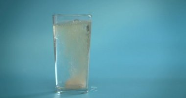 C vitamini tableti şeffaf bir bardağa suyla atılır. Parlak pembe tablet erir. Mavi arka planda cam var. Yavaş çekim