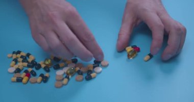 Elinde haplar, haplar, vitaminler, uyuşturucular, mavi arka planda izole edilmiş kapsüller olan bir erkek eli. Coronavirus tedavisi konsepti. Sağlık hizmeti konsepti. İlaç endüstrisi..