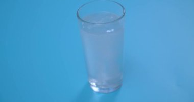 C vitamini tableti şeffaf bir bardağa suyla atılır. Parlak pembe tablet erir. Mavi arka planda cam var. Yavaş çekim