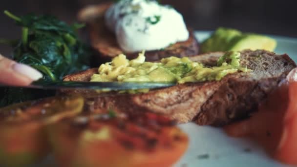 Close-up shot of making a healthy snack with dark rye bread and avocado spread with grilled tomato and a poached egg. Breakfast in Bali Indonesia — Stock Video