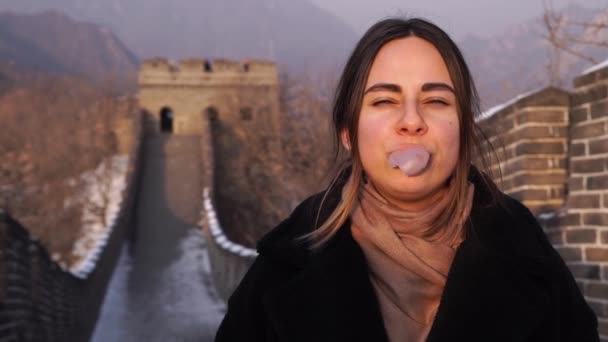 Mädchen kaut und platzt auf der großen Mauer vor chinesischem Hintergrund — Stockvideo