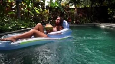 Güzel bir kadın, gün batımında havuz kenarında lüks bir sahil otelinin kaplıcasında dinleniyor. Mükemmel bir plaj tatili ve seyahat görüntülerinin keyfini çıkarıyor.