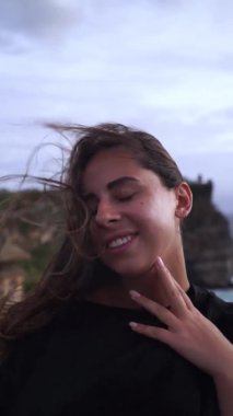 Güzel kar beyazı bir gülüşü olan, rüzgarda duran bir kadının yakın portresi. Esinti bir kızın saçıyla oynar. Dikey video