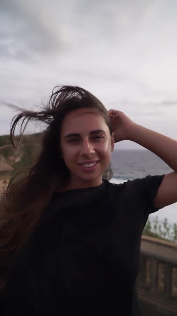 Närbild porträtt av en kvinna med ett vackert snövitt leende, stående i vinden. Breeze leker med en flickas hår. Vertikal video — Stockvideo