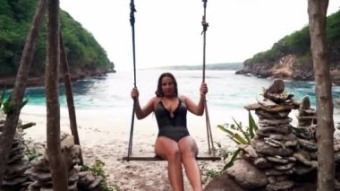 Deniz sahilinde salıncakta sallanan mutlu kadın. Genç kız yaz tatilinde salıncakta sallanıyor. Yaz tatilinde eğleniyorum. Genç mutlu insanlar yaşam tarzı. Tropik sahil yaşam tarzı